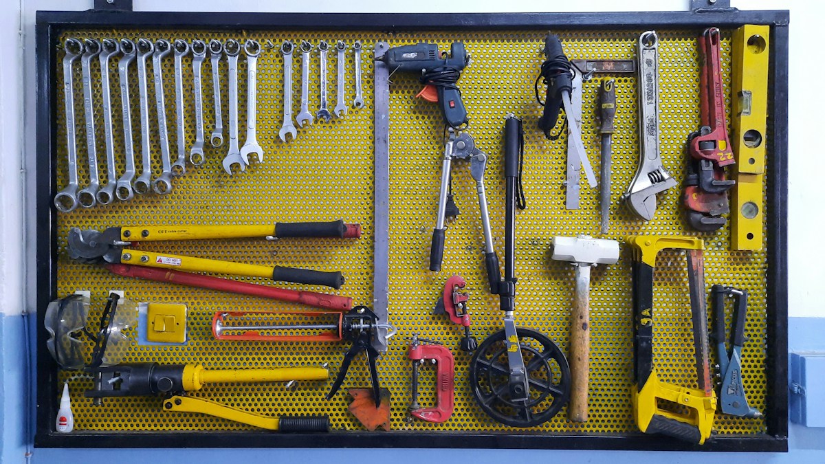 Panneau perforé jaune avec nombreux outils de bricolage suspendus.